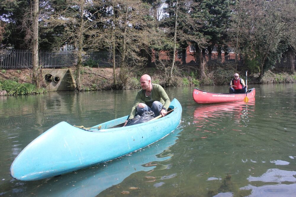 A Save Our Stort volunteer collecting litter from a canoe on the River Stort, with another paddler close behind